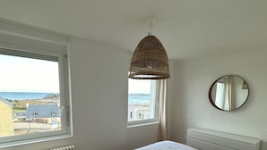 Una camera da letto con un'ampia finestra, un letto, un comodino, una lampada, uno specchio e una luce a soffitto.