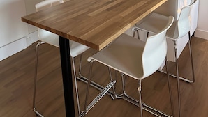 Una cucina moderna con un piano di lavoro in legno, sedie bianche, una cappa aspirante nera e una macchina per il caffè.