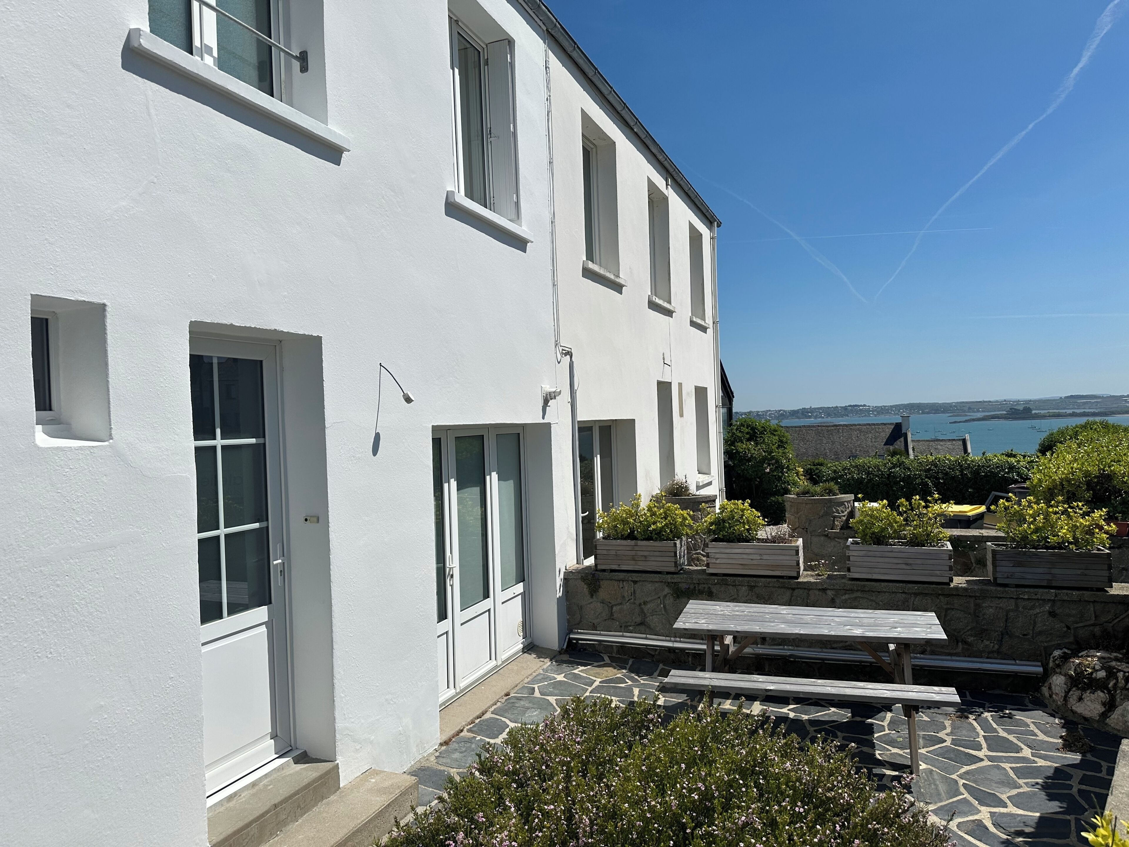 Un bâtiment blanc doté de nombreuses fenêtres et d’une terrasse en pierre avec des bancs.