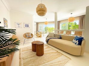 Un salon moderne avec un canapé beige, une table basse ronde en bois et une grande fenêtre donnant sur un paysage verdoyant.