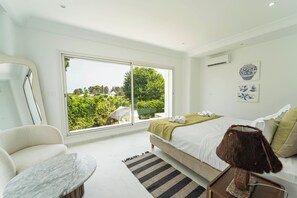 A modern hotel room with a large sliding glass door, a bed with a green throw, a marble side table, and a view of greenery outside. - Villa Punique: Villa exceptionnelle avec vue mer (Site archéologique de Carthage)