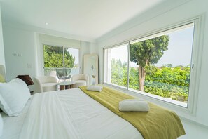 A modern hotel room with a large bed, a seating area, and a view of greenery. - Villa Punique: Villa exceptionnelle avec vue mer (Site archéologique de Carthage)