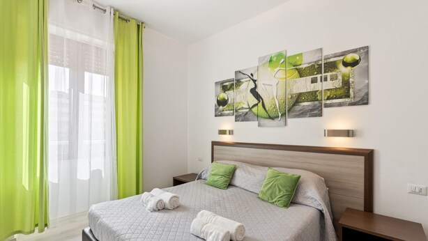 Habitació d'hotel amb un llit, cortines verdes, un melic, una tauleta de nit i decoració mural.