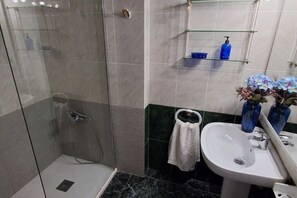 Une salle de bain avec une douche à parois de verre, un lavabo blanc et un miroir. On y trouve des vases bleus sur le lavabo et une serviette accrochée au mur.