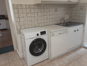 Eine kleine Küche mit Waschmaschine, Spüle und Fliesen.