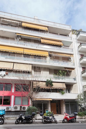 A multi-story building with balconies, air conditioning units, and a red storefront. - Trendy Cozy 2 Bd Apt in Panormou Metro Station (Athina)