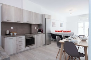 A modern kitchen with light wood cabinets, stainless steel appliances, and a dining area with a table set for two. - Trendy Cozy 2 Bd Apt in Panormou Metro Station (Athina)