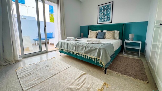 Ein Schlafzimmer mit Bett, Nachttisch, einem gerahmten Bild und Blick durch eine Schiebetür.