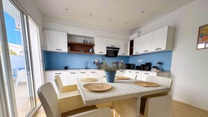 Eine moderne Küche mit weißen Schränken, einer blauen Arbeitsplatte und einem Essbereich mit Korbstühlen und einem weißen Tisch.