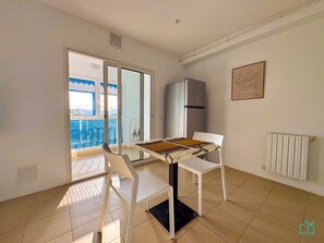 A room with a dining table, two chairs, a refrigerator, and a radiator. - Coste Sidi Bou Said A3: Spacious and central (Site archéologique de Carthage)