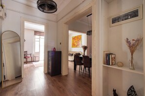 Ein geräumiges Zimmer mit Holzboden, einer Essecke mit Stühlen und Tisch, einem Bücherregal und einem gerahmten Bild an der Wand.
