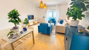 Ein modernes Wohnzimmer mit Essbereich, blauen Sofas, einem Fernseher und Topfpflanzen.
