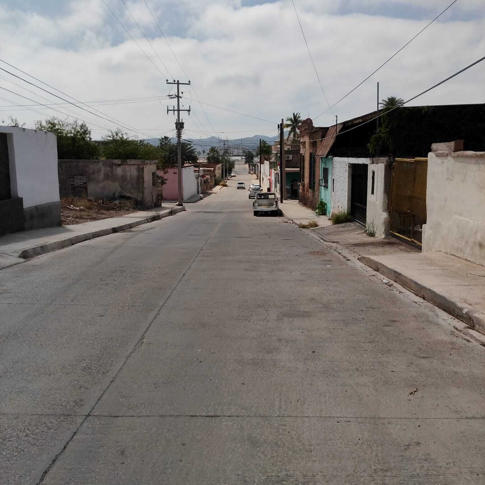 Une rue tranquille, bordée de bâtiments des deux côtés, avec une voiture garée sur le bord et des lignes électriques qui la surplombent.