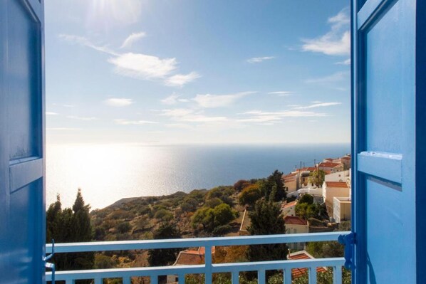 A view from a balcony with a railing, overlooking a coastal town with buildings and trees, and the sea in the background.