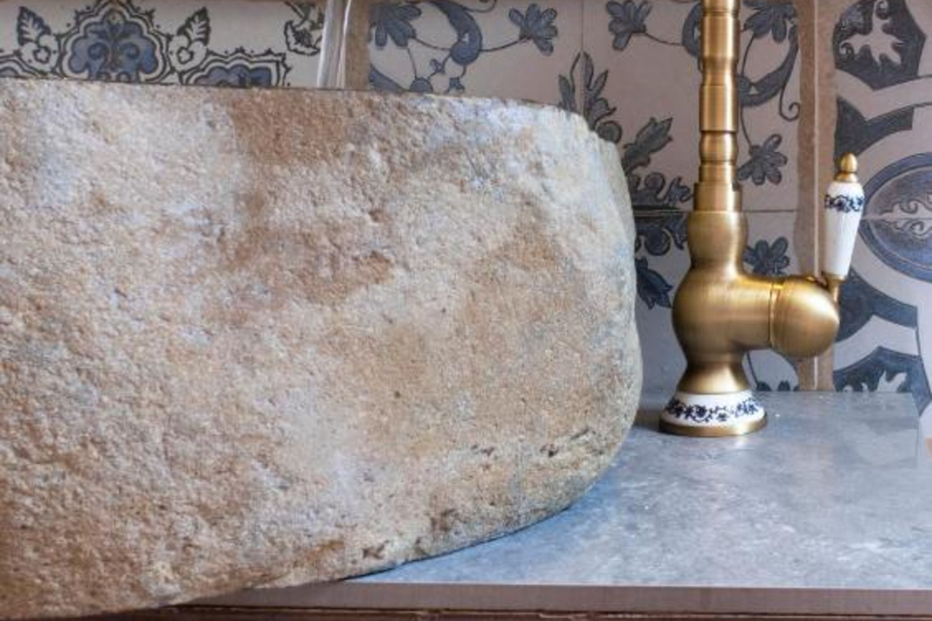 A stone sink with a brass faucet and a decorative vase.