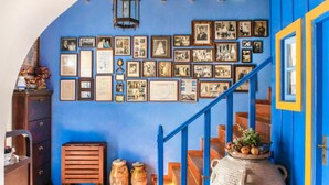 Una habitación con una pared azul decorada con fotografías enmarcadas, una escalera de madera con barandillas azules y una maceta de cerámica grande en el suelo.