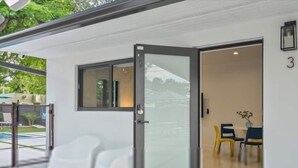 Een modern gebouw met een glazen deuropening, een klein terras met twee witte stoelen, en het getal '3' op de muur.