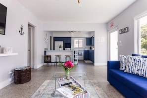 A modern living room with a blue sofa, a coffee table with magazines, and a kitchen in the background. - Peaceful Beach Oasis with Free Parking (Hollywood)