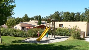 Un’area giochi con uno scivolo giallo e strutture per arrampicarsi, circondata da un prato curato e alberi.