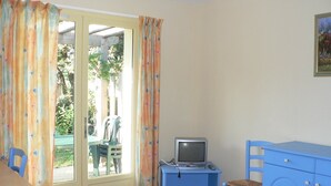 Una stanza con una porta scorrevole in vetro, una piccola TV su un mobiletto blu, una sedia blu e un armadietto blu.