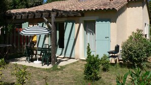 Una casa rustica con tetto in tegole, un patio coperto con un ombrellone a righe e un piccolo giardino.