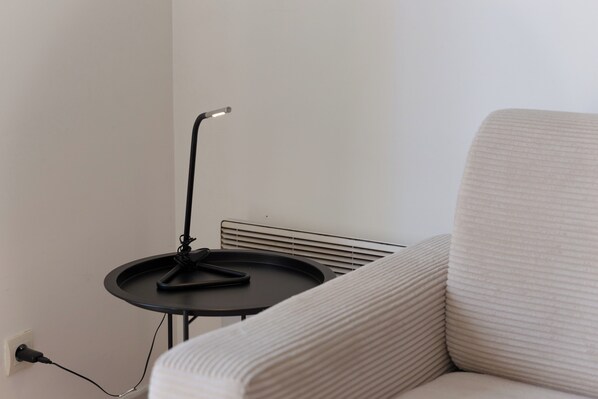 Une pièce moderne avec un canapé blanc, une petite table noire avec une lampe et une prise de courant au mur.