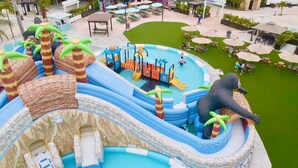 Een opblaasbaar waterpark met glijbanen en een zwembad, omringd door terrasstoelen en palmbomen.
