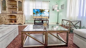 Een woonkamer met een televisie, een glazen salontafel, een bank, een kast en een vloerlamp.