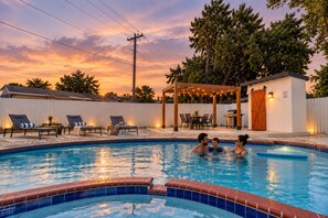 A swimming pool with a brick edge, surrounded by lounge chairs and a covered patio area. - NEW! Luxury 5BR Villa*Private Pool*BBQ*Game Room (Miami Gardens)