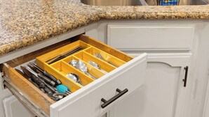 Uma cozinha com bancada de granito, pia de aço inoxidável e gaveta para utensílios de madeira.