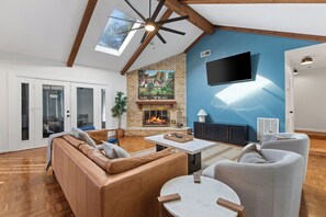 A spacious living room with a fireplace, leather sofa, and a flat-screen TV mounted on the wall. - Heater Pool! 10 beds-4 K beds, Games, Gym, Theater (San Antonio)