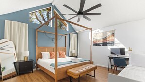 Um quarto com cama de dossel, escrivaninha com computador e ventilador de teto.