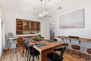 A modern kitchen with wooden cabinets, a dining area with a large table and bar stools, a high ceiling with a geometric light fixture, and a large framed picture on the wall. - Heater Pool! 10 beds-4 K beds, Games, Gym, Theater (San Antonio)