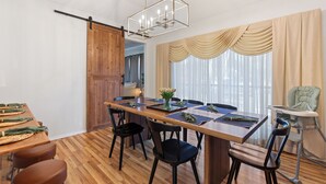 Uma sala de jantar com mesa de madeira, cadeiras, teto alto e porta deslizante.