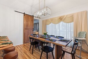Un comedor con mesa de madera, sillas, techo alto y puerta corredera.