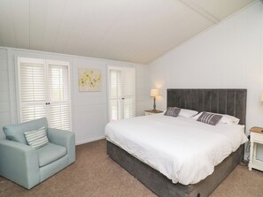 A bedroom with a large bed, a light blue armchair, and white walls.