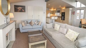 A living room with a light blue sofa, a grey sofa, a coffee table, a fireplace, and a kitchen area visible through an open door. - Indulgence Fishing Lodge With Private Hot Tub (Lincoln)