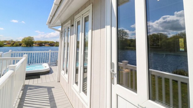 A deck with a hot tub, a view of a lake, and a building with large windows. - Indulgence Fishing Lodge With Private Hot Tub (Lincoln)