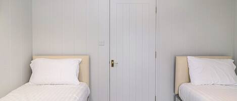 Une chambre avec deux lits simples, une porte blanche et un sol recouvert de moquette.