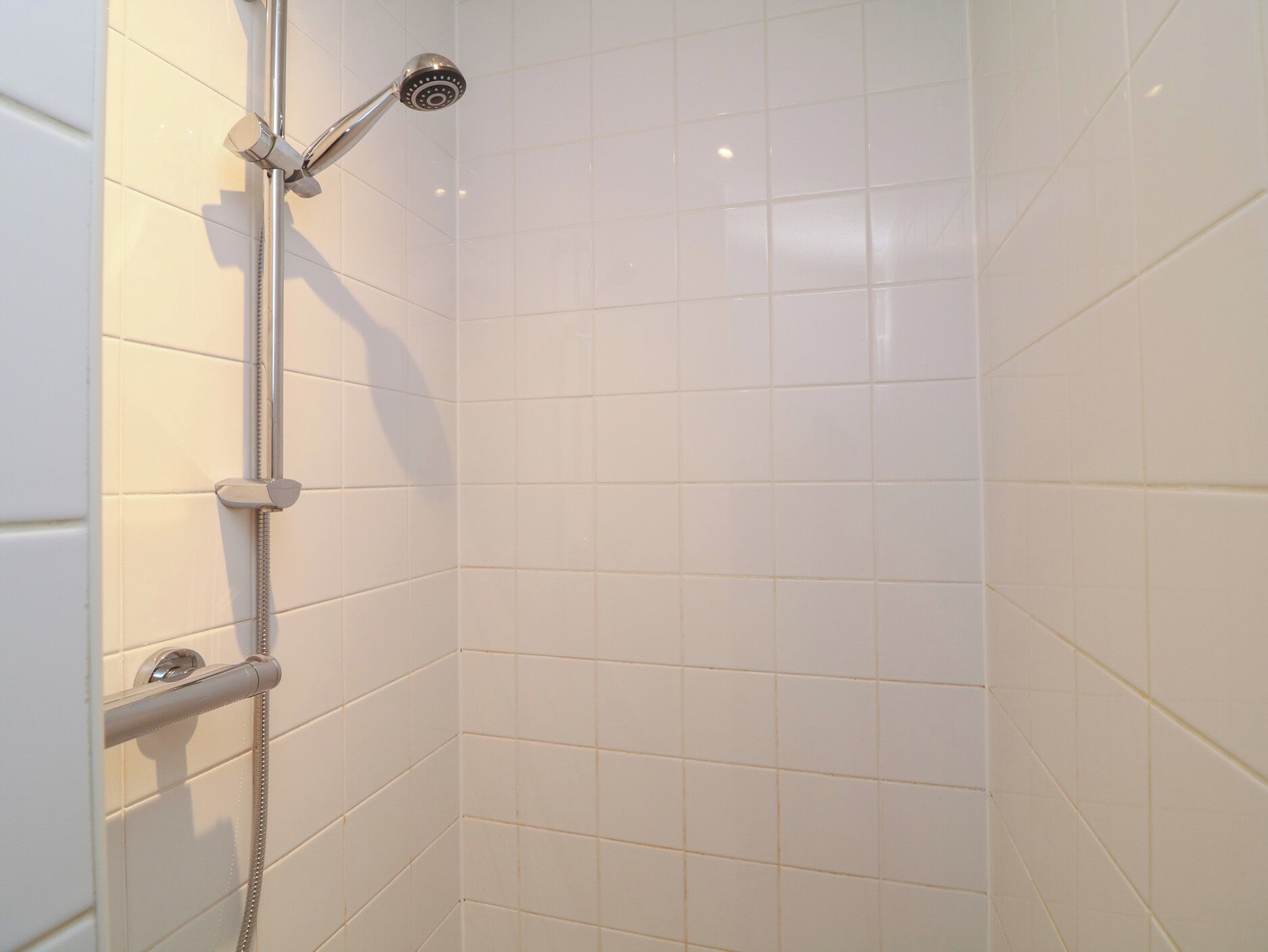 A shower with a handheld showerhead, a wall-mounted faucet, and a control knob.