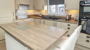 A modern kitchen with light-colored cabinets, a wooden countertop, a built-in oven, and a window with a roller blind. - Indulgence Fishing Lodge With Private Hot Tub (Lincoln)