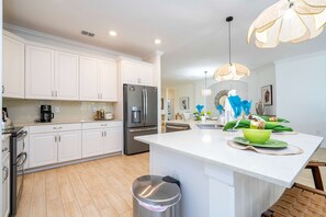 Una cocina moderna con armarios blancos, electrodomésticos de acero inoxidable y una isla central con un bol verde.