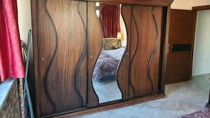 Un dormitorio con un armario de madera grande, una cama con cubrecama estampado y una cortina roja.