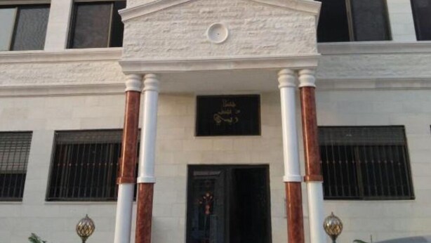 Un edificio con una entrada central flanqueada por columnas, varias ventanas y una cúpula decorativa.