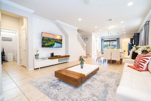 A modern living room with a white sofa, a coffee table, and a TV mounted on the wall. - Gorgeous 5Bd w Private Pool Windsor Westside 8893 (Kissimmee)