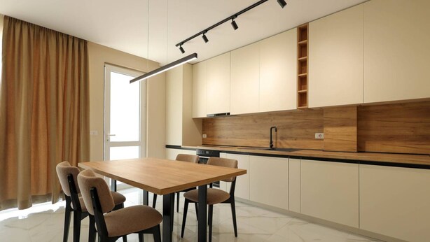 A modern kitchen with a wooden countertop, built-in cabinets, and a dining area with a table and chairs. - SanPietro Vacation Apartment 023 (Plazhi San Pietro)