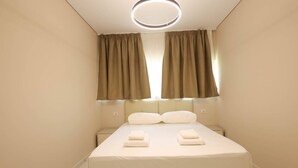 A neatly made bed with white linens and two folded towels, a bedside table, and a modern ceiling light fixture. - SanPietro Vacation Apartment 023 (Plazhi San Pietro)