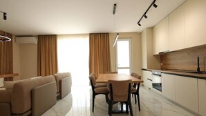 A modern living room with a sofa set, a dining table with chairs, and a kitchen area with a wooden countertop and cabinets. - SanPietro Vacation Apartment 023 (Plazhi San Pietro)