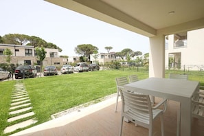 A patio area with a table and chairs, a grassy lawn, and parked cars. - SanPietro Vacation Apartment 022 (Plazhi San Pietro)