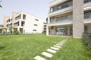 Un immeuble résidentiel moderne à plusieurs étages, doté de balcons, d’une pelouse bien entretenue et surplombant un ciel dégagé.